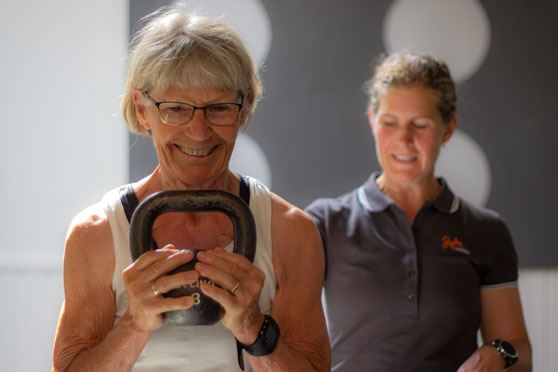 Personlig tränare instruerar en person som lyfter en kettlebell.
